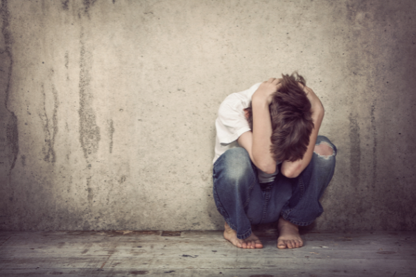 person huddled, slumped down in a ball leaning against concrete wall, crying guilt and shame